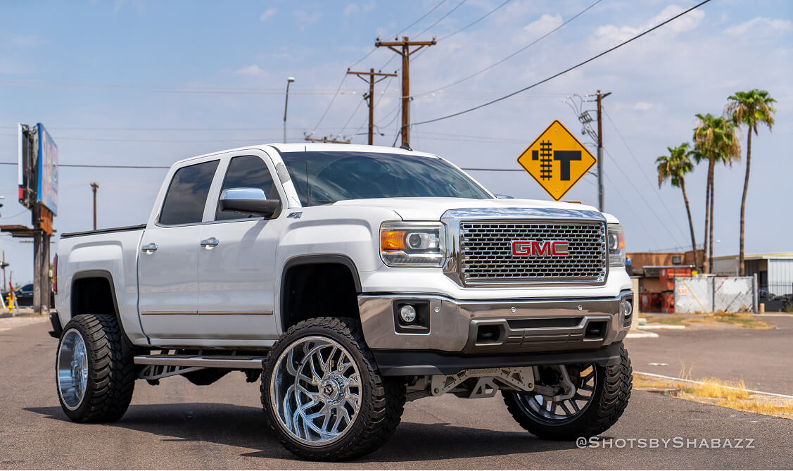 White GMC pickup with raised suspension and aftermarket wheels